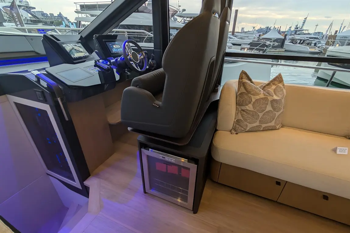 Modern boat interior featuring a sleek dashboard, captain's seat, and a beige sofa with a decorative leaf-patterned cushion.